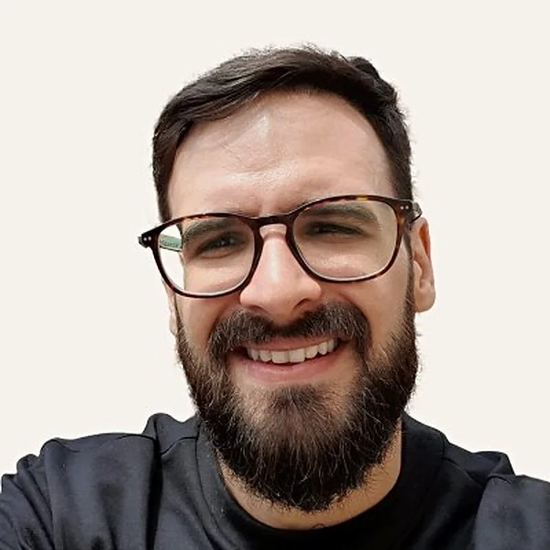Retrato de Mário Sérgio Dias, sorrindo, de óculos e barba
